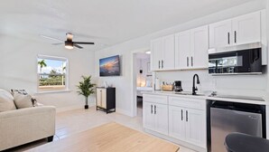 A modern kitchen with white cabinets, a microwave, and a dishwasher. There is a dining area with a table and chairs, and a ceiling fan. - Las Olas of Treasure Island No. 1 (Treasure Island)