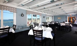 Enjoy meals with a view of the sea from our dining area, featuring tables set with white tablecloths and comfortable seating.