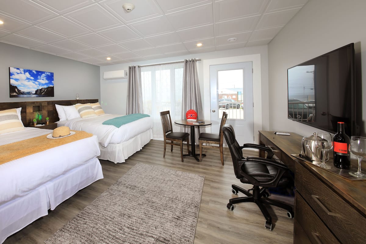 A hotel room with two beds, a dining table, chairs, a TV, and a bottle of wine.
