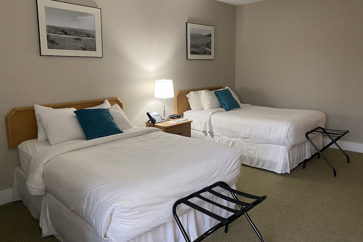 A hotel room with two beds, a nightstand with a lamp, and a small table.