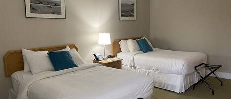 A hotel room with two beds, a nightstand with a lamp, and a small table.