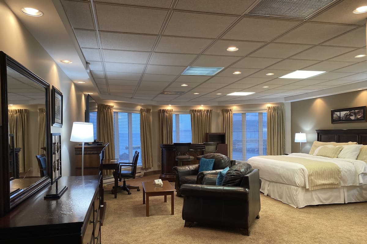 A hotel room with a large bed, a desk with a chair, a leather sofa, and a TV.