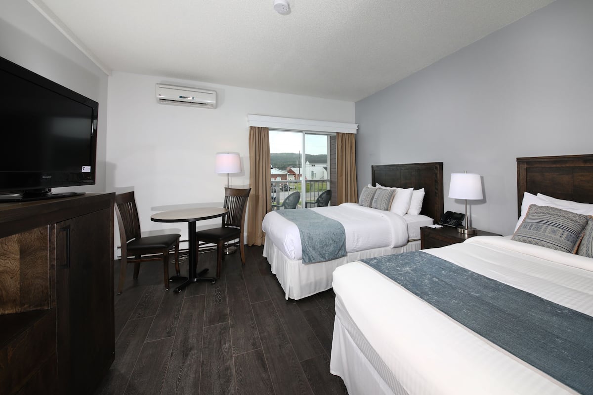A hotel room with two beds, a desk with a chair, a television, and a window with curtains.
