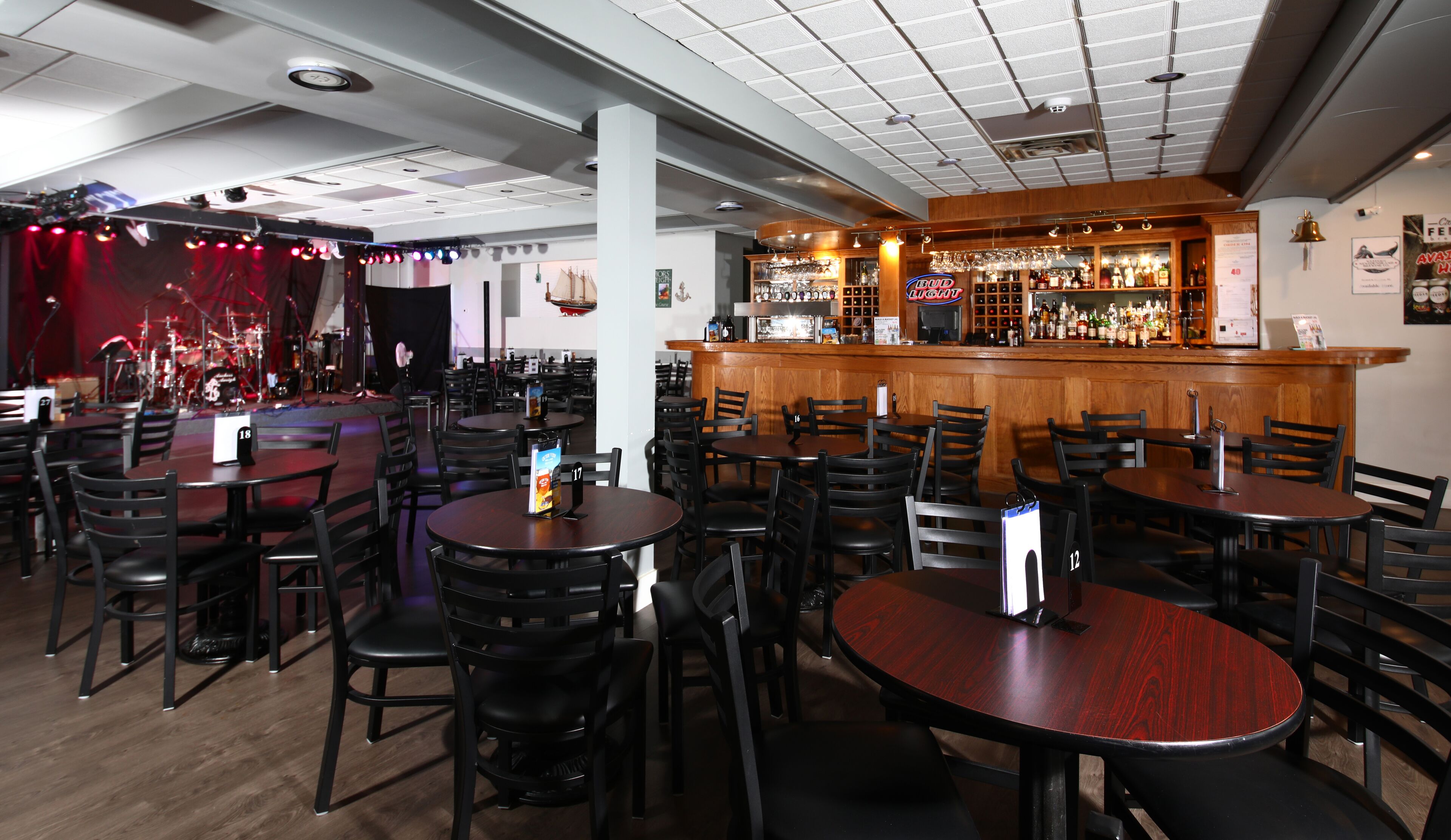 Ein Restaurant mit mehreren runden Tischen und Stühlen, einer Bar mit einer Holztresen und einer Bühne mit roten Vorhängen im Hintergrund.