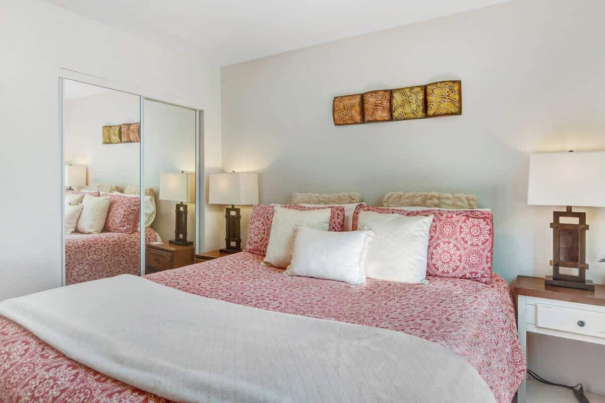 A bedroom with a large bed, a mirror, bedside lamps, and a wall-mounted artwork.