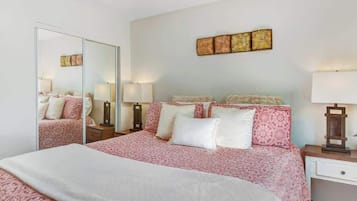 A bedroom with a large bed, a mirror, bedside lamps, and a wall-mounted artwork.