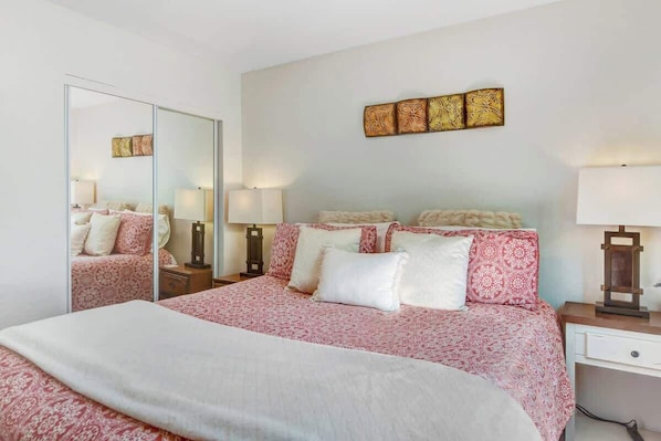 A bedroom with a large bed, a mirror, bedside lamps, and a wall-mounted artwork.