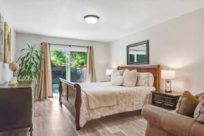 A bedroom with a bed, bedside tables, a lamp, a dresser, a plant, and a view of the outdoors.