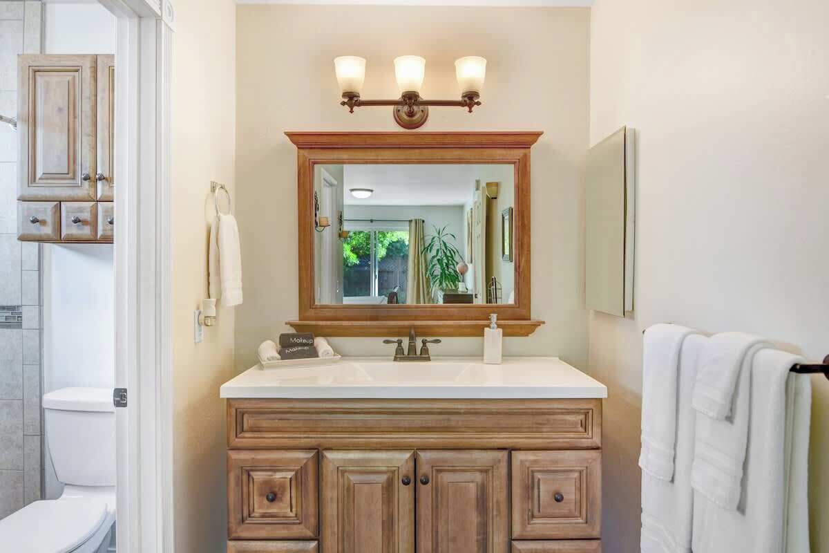 A bathroom with a wooden vanity, a mirror with lights, and a towel rack.