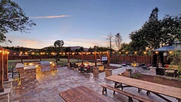 Un espace extérieur aménagé en terrasse, avec un sol en pierre, des meubles en bois et des guirlandes lumineuses.