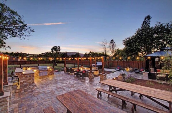 Un espace extérieur aménagé en terrasse, avec un sol en pierre, des meubles en bois et des guirlandes lumineuses.