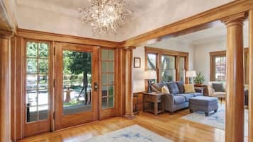Un salon spacieux agrémenté d’un grand lustre, d’un parquet en bois et offrant une vue sur l’extérieur grâce à de grandes fenêtres.