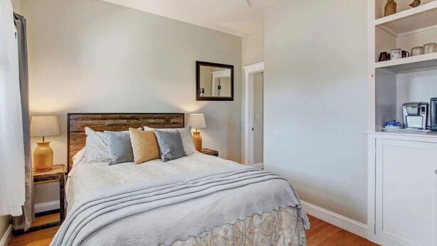 Une chambre à coucher avec un lit, des lampes de chevet, un miroir et une armoire blanche contenant des ustensiles de cuisine.