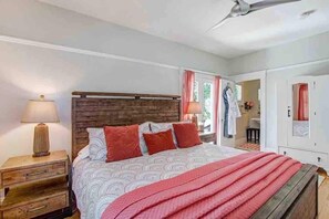 A bedroom with a wooden headboard, a bed with patterned bedding, a red throw blanket, a nightstand with a lamp, and a wardrobe.
