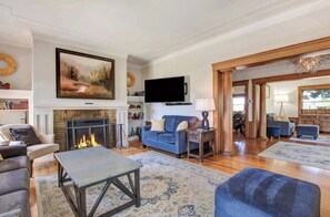 Amplia sala de estar con chimenea, televisor de pantalla plana grande montado arriba y un espacio de asientos cómodo con sofás y una mesa de centro.