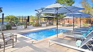 Une piscine entourée d’un mur de briques et d’arbres, avec des chaises longues et des parasols.