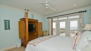 Een slaapkamer met een groot bed, een houten kast met een televisie en uitzicht op het strand door het raam.
