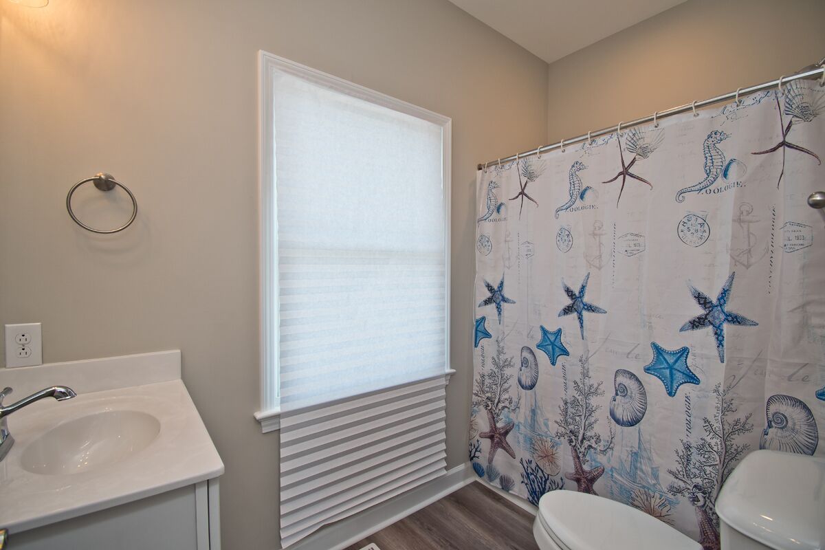 A bathroom with a white sink, toilet, and shower curtain with a seashore design.