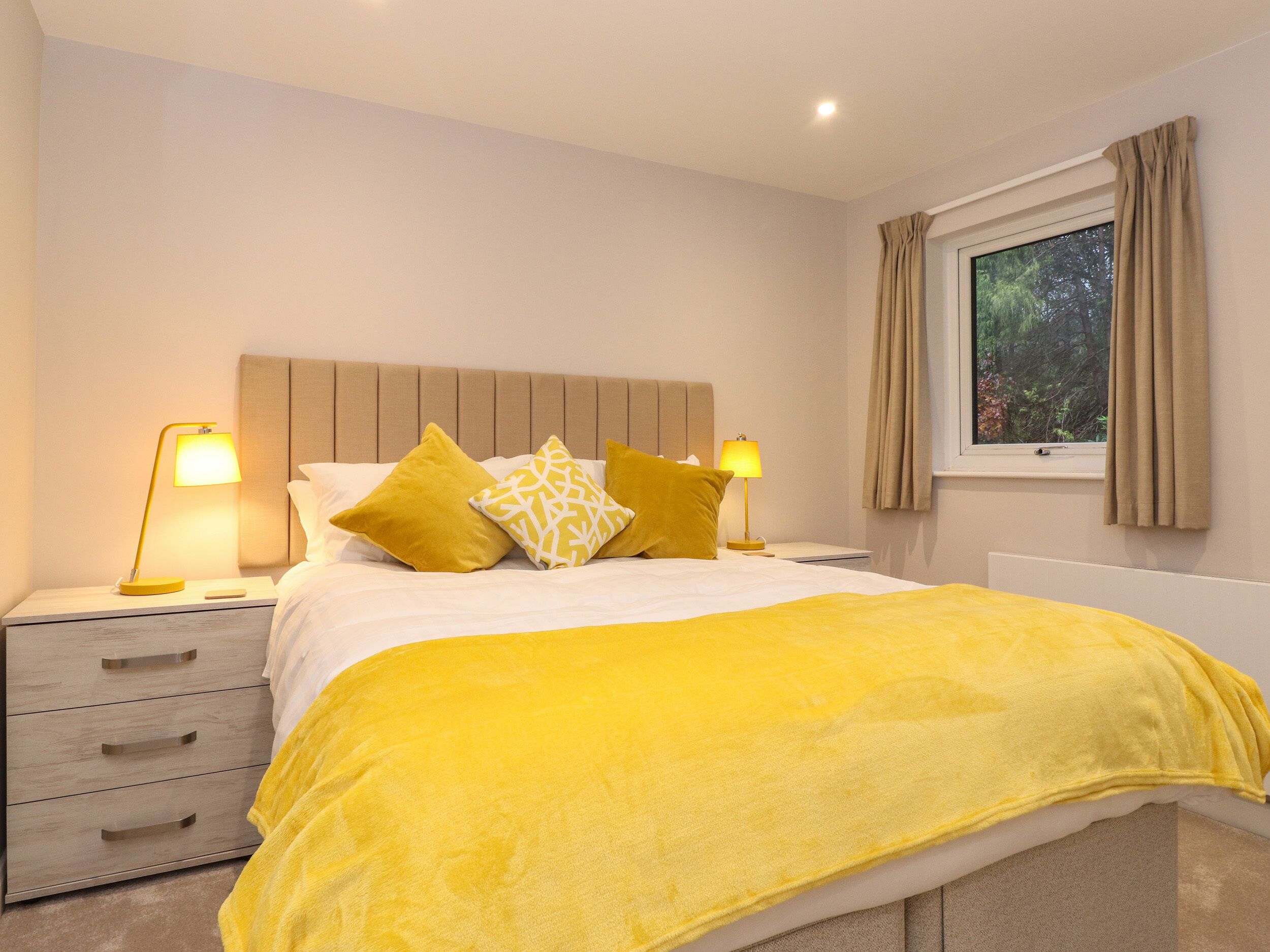 A modern bedroom with a bed, two bedside lamps, a nightstand, and a window with curtains.