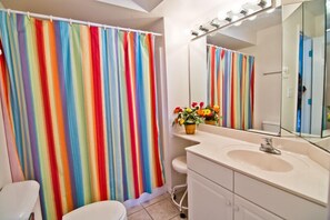A bathroom with a colorful striped shower curtain, a sink with a mirror, and a small flower arrangement on the counter. - Viewpoint, Oceanfront House in Emerald Isle, NC! (Emerald Isle)