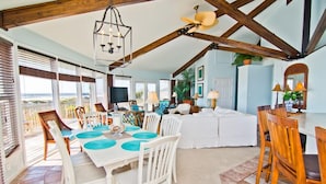 A spacious living area with a dining table set for six, a ceiling fan, and a large window offering a view of the outdoors. - Viewpoint, Oceanfront House in Emerald Isle, NC! (Emerald Isle)