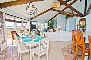 A spacious living area with a dining table set for six, a ceiling fan, and a large window offering a view of the outdoors.