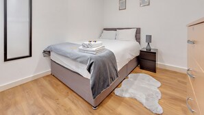 A bedroom with a bed, bedside table, lamp, and a white fur rug. - Central London apartment (London)