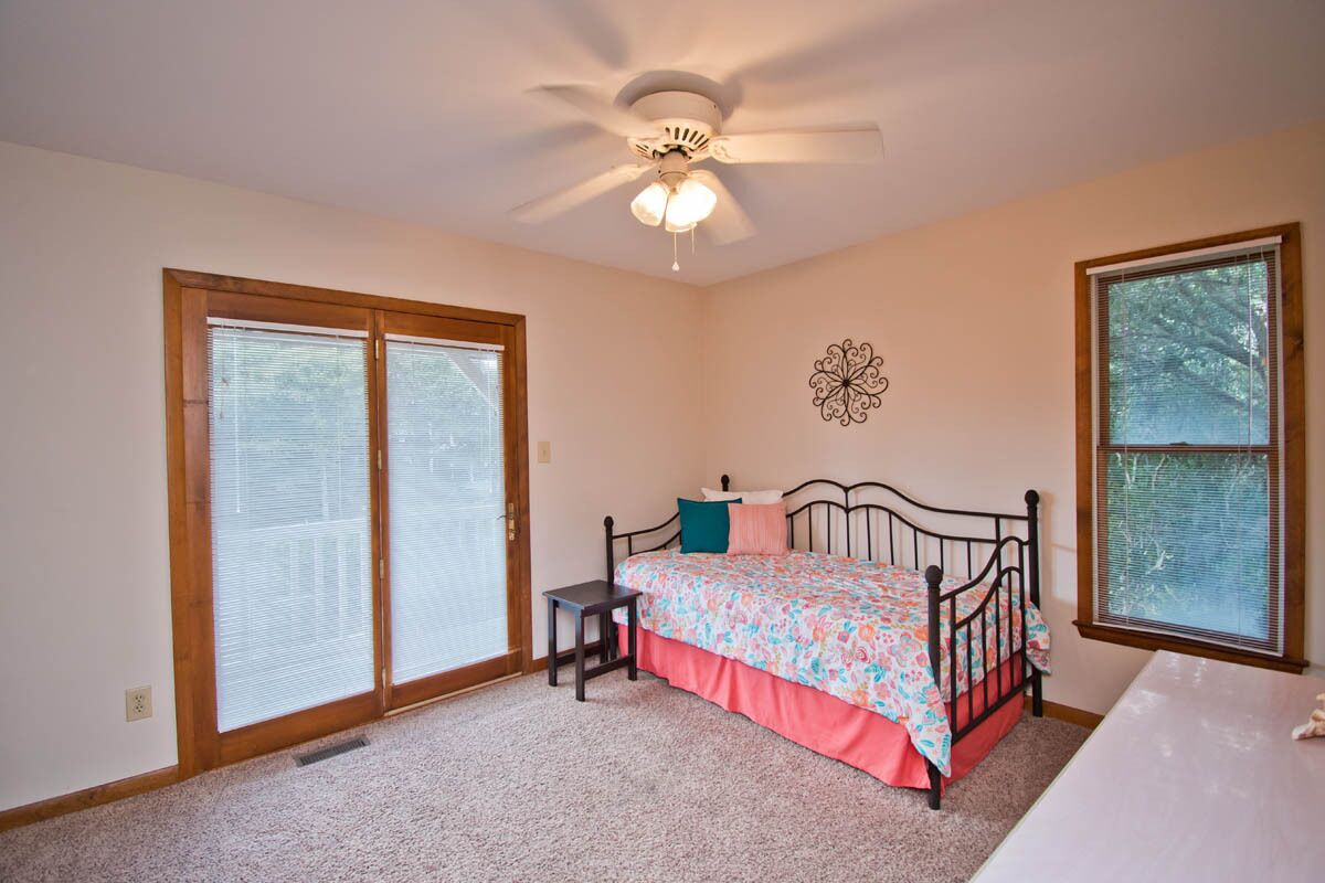 A bedroom with a bed, a ceiling fan, a decorative wall piece, and a window.