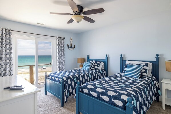 Une chambre avec deux lits, un ventilateur de plafond et vue sur la plage.