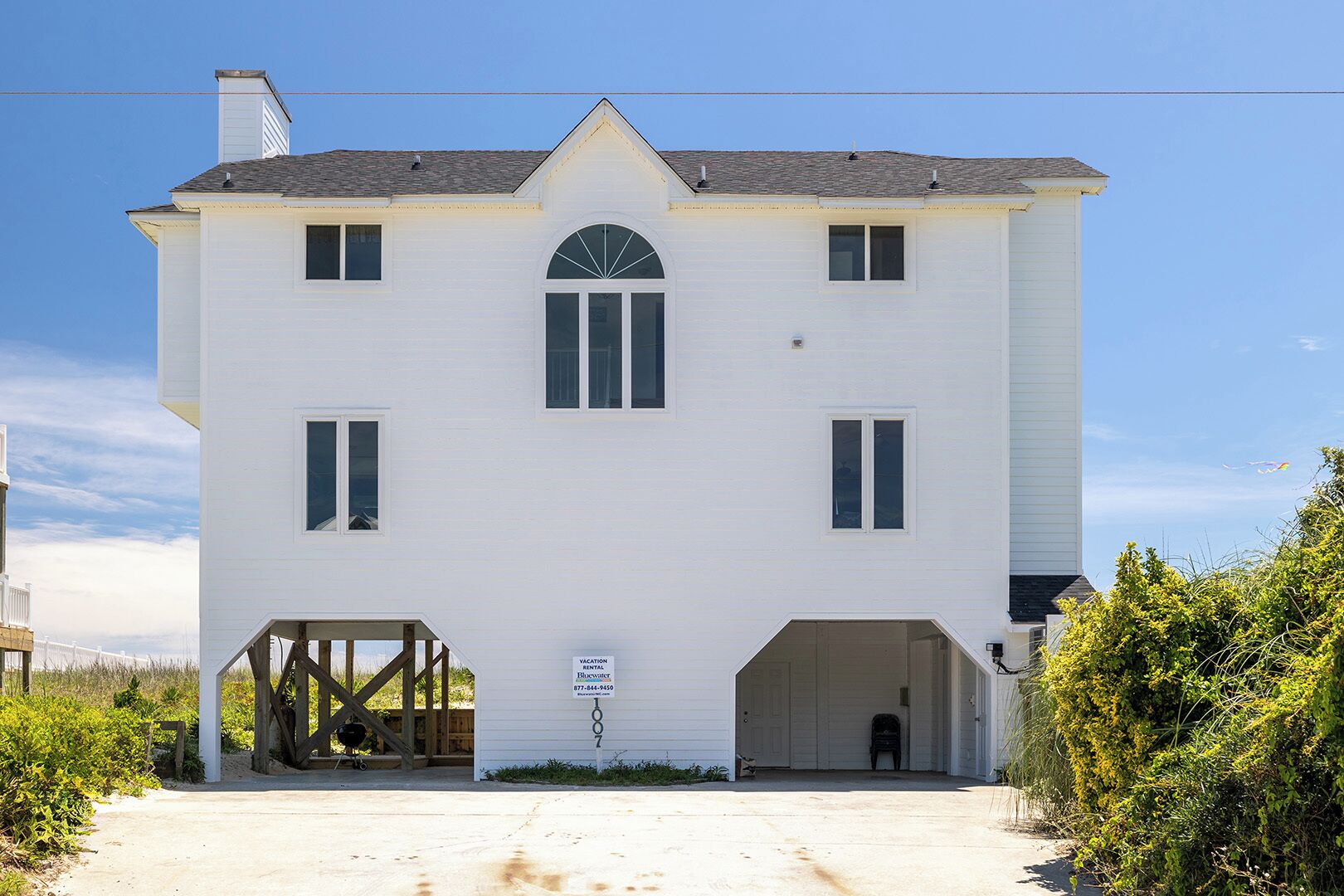 A large white two-story building with a central arched window, a covered porch, and a sign indicating vacation rental availability.