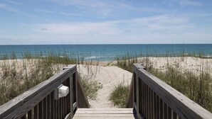 Ein hölzerner Steg führt zu einem Strand mit Dünen und Meerblick.
