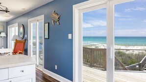 Ein Zimmer mit einer großen Schiebeglasdoor, die auf eine Holzterrasse mit Blick auf einen Strand führt.