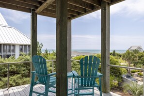 A wooden deck with two chairs and a table, overlooking a coastal landscape with houses and vegetation. - Bonnie Banks, Almost Oceanfront House in Emerald Isle, NC! (Emerald Isle)