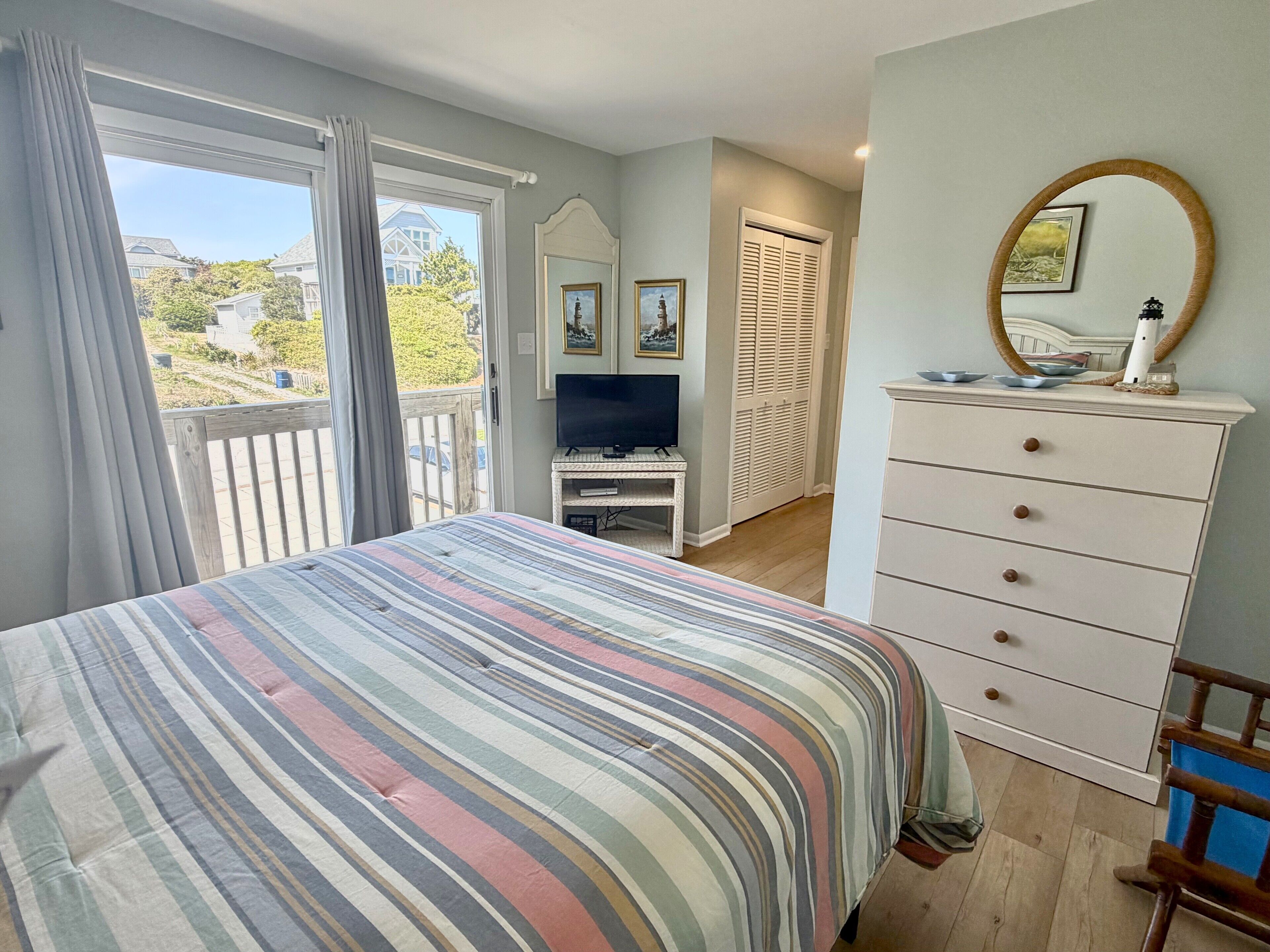 A bedroom with a bed, a dresser, a television, and a balcony.