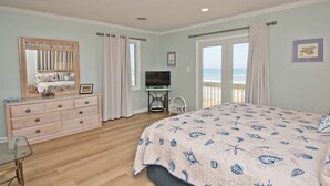 Een slaapkamer met een bed, dressoir, televisie en uitzicht op de oceaan.