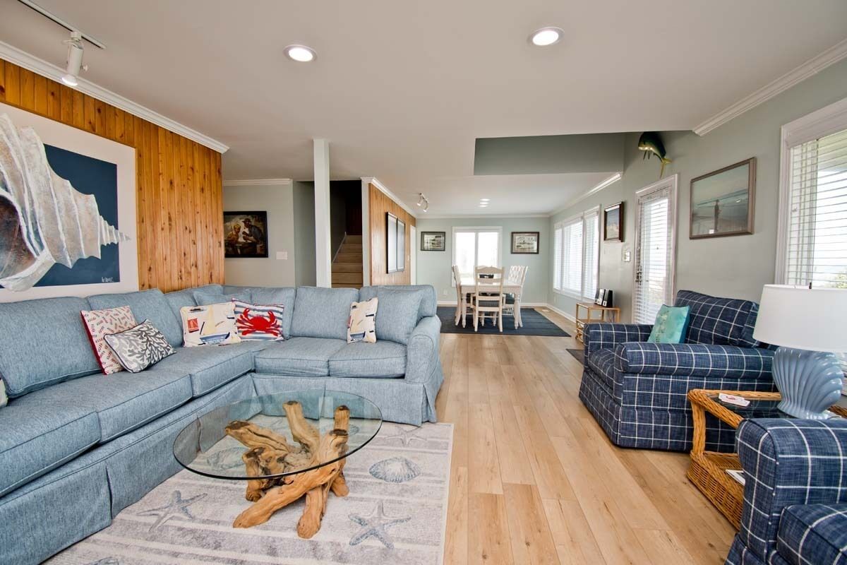 A spacious living room with a sectional sofa, a glass coffee table, and a blue plaid sofa.