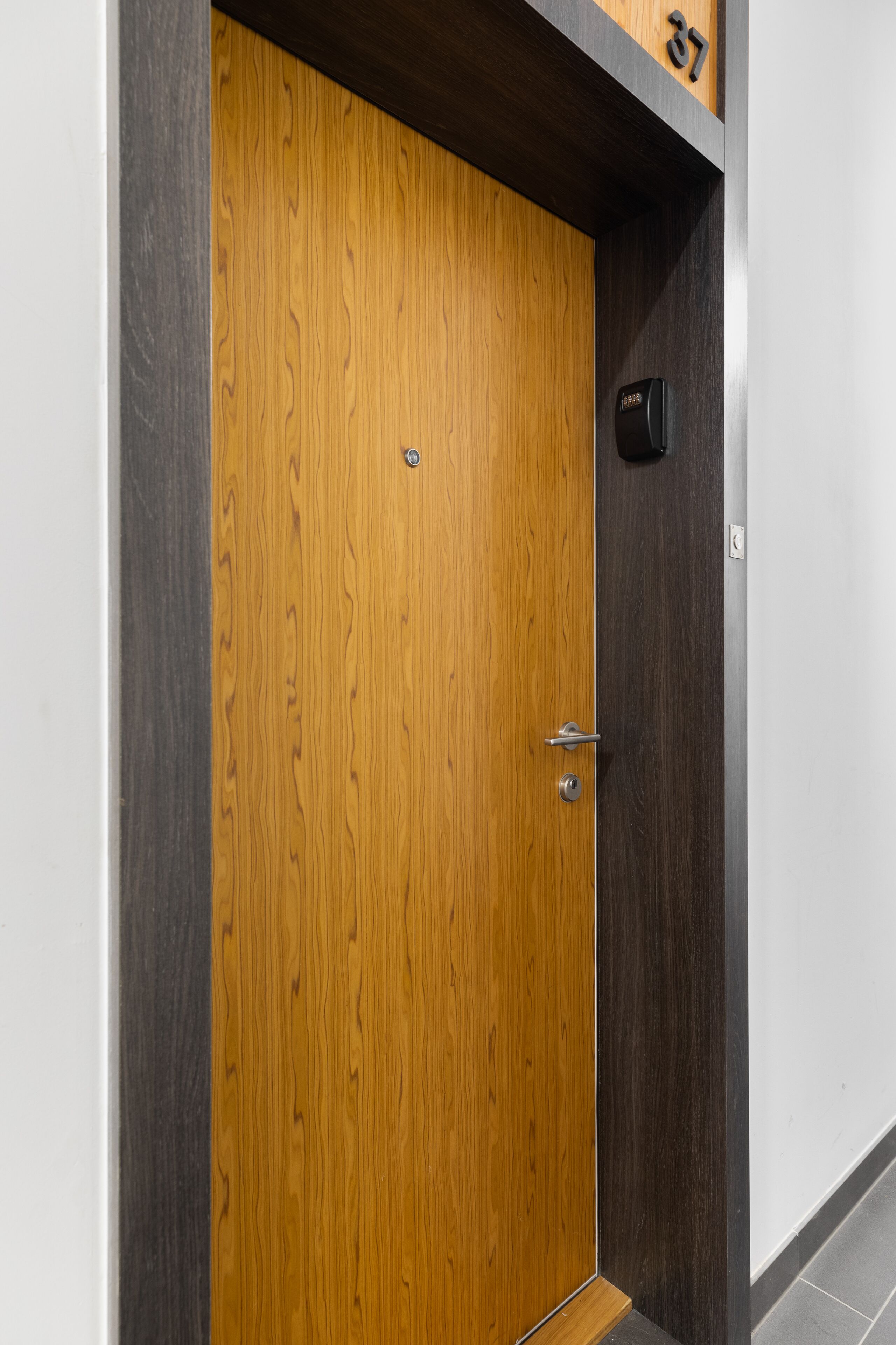A wooden door with a handle and a small lock, a dark wall, and a number "37" above it.