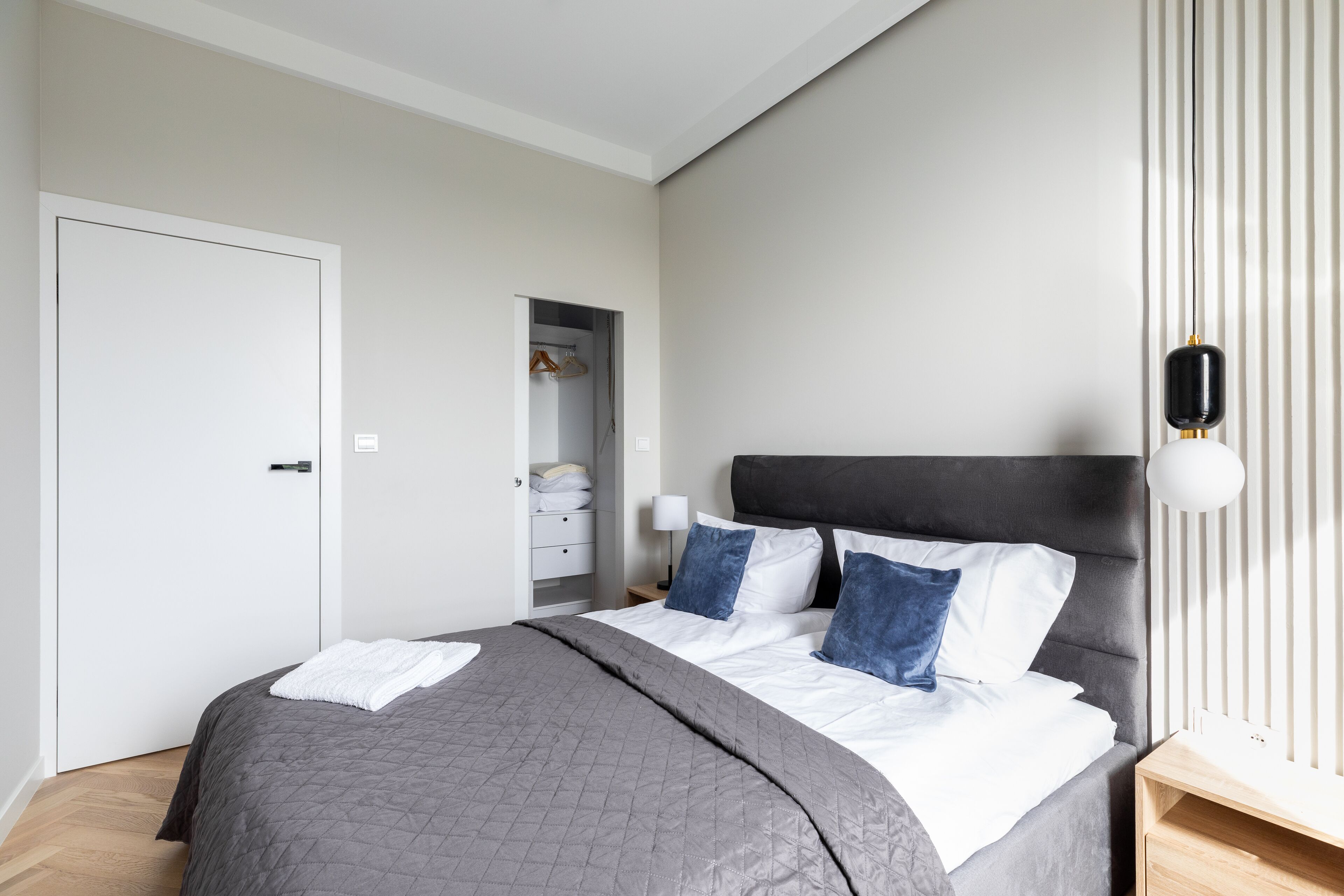 A modern bedroom with a large bed, a wardrobe, and a bedside table.