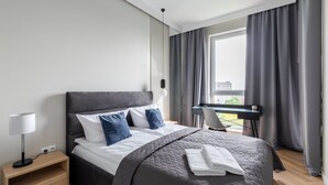 Moderni hotellihuone, jossa on suuri sänky, työpöytä ja näkymä ulos.