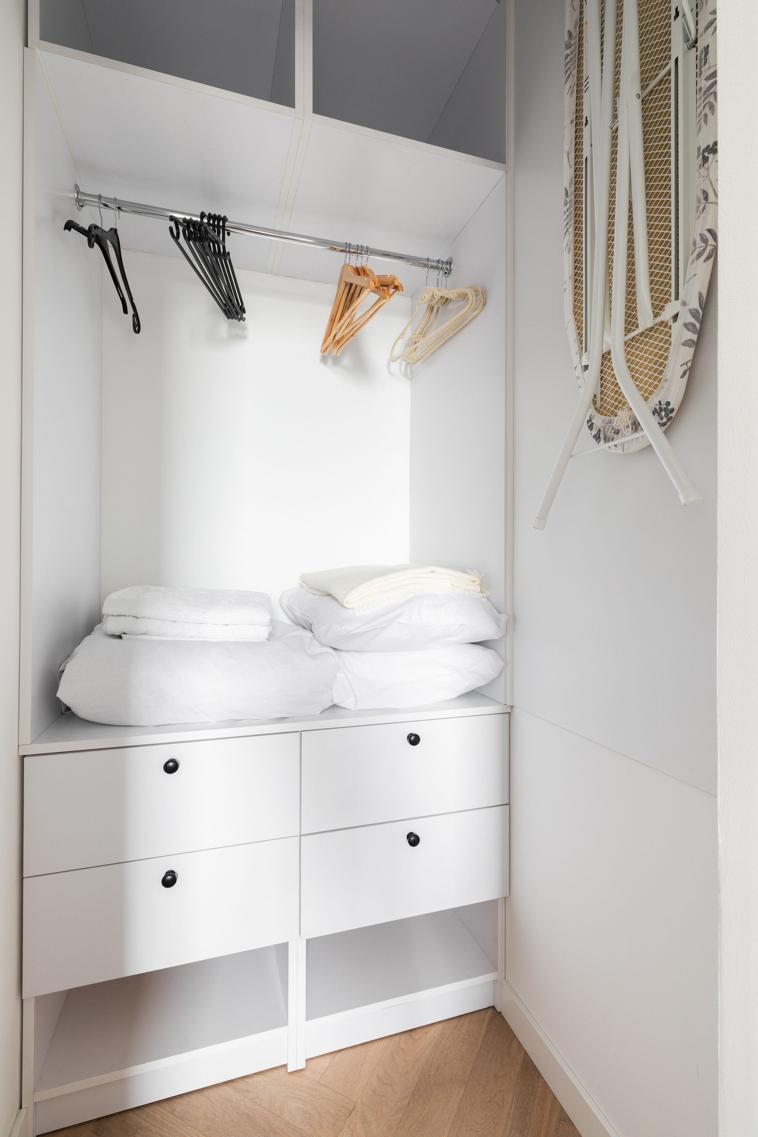 A white closet with hanging space, a folded towel rack, and a mirror.