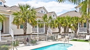 A pool area with a clear blue pool, white railings, and palm trees. - Bungalows At The Grove #6, Oceanside House in Atlantic Beach, NC! (Atlantic Beach)