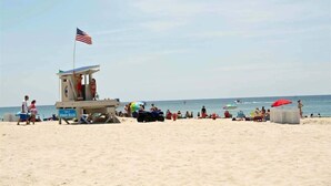 A lifeguard tower with an American flag, beach umbrellas, and people relaxing on the sand. - Bungalows At The Grove #6, Oceanside House in Atlantic Beach, NC! (Atlantic Beach)