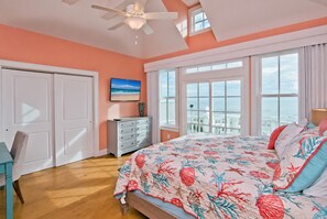 Un dormitorio con una cama grande, un aparador, un televisor y un balcón con vistas al océano.