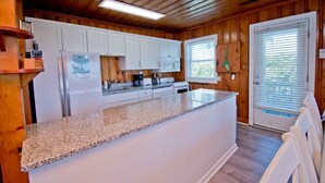 A kitchen with wooden paneling, white cabinets, a granite countertop, and a built-in microwave. - Captain's Escape, Almost Oceanfront House in Emerald Isle, NC! (Emerald Isle)