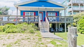 A beach house with a blue exterior, numbered 2412, featuring a wooden deck and a porch with chairs. - Captain's Escape, Almost Oceanfront House in Emerald Isle, NC! (Emerald Isle)