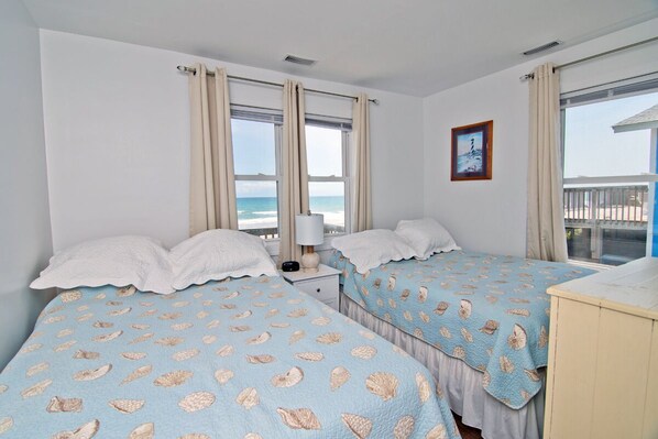 A bedroom with two beds, a nightstand, a lamp, and a view of the ocean.