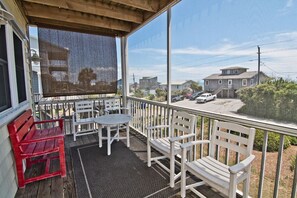 A covered porch with white and red benches, a table, and a view of a residential street. - Cardinal's Landing, Almost Oceanfront House in Emerald Isle, NC! (Emerald Isle)