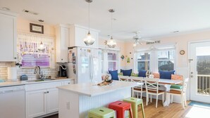 A kitchen with white cabinets, a central island, and a dining area with a table and chairs. - Cardinal's Landing, Almost Oceanfront House in Emerald Isle, NC! (Emerald Isle)