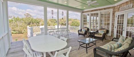 A covered outdoor area with a table and chairs, a wicker sofa, and a ceiling fan.
