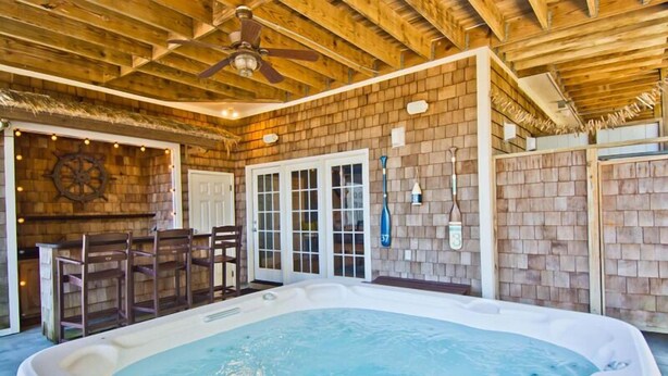 Een hottub in een rustieke chalet met houten wanden, een plafondventilator en een bar met stoelen.